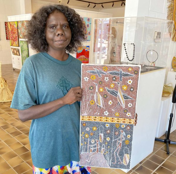 Jay Jurrupula holding a painting of birds and people, Aboriginal artist in Songlines Gallery Darwin